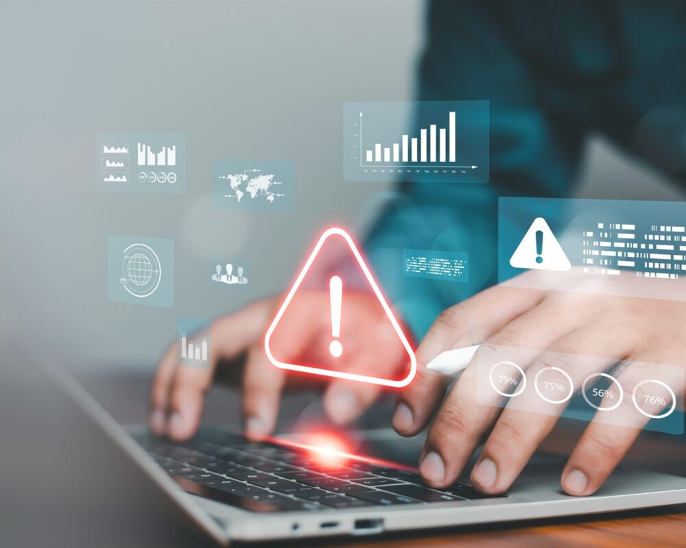 Employee typing on a laptop with a security warning alert and risk data overlays
